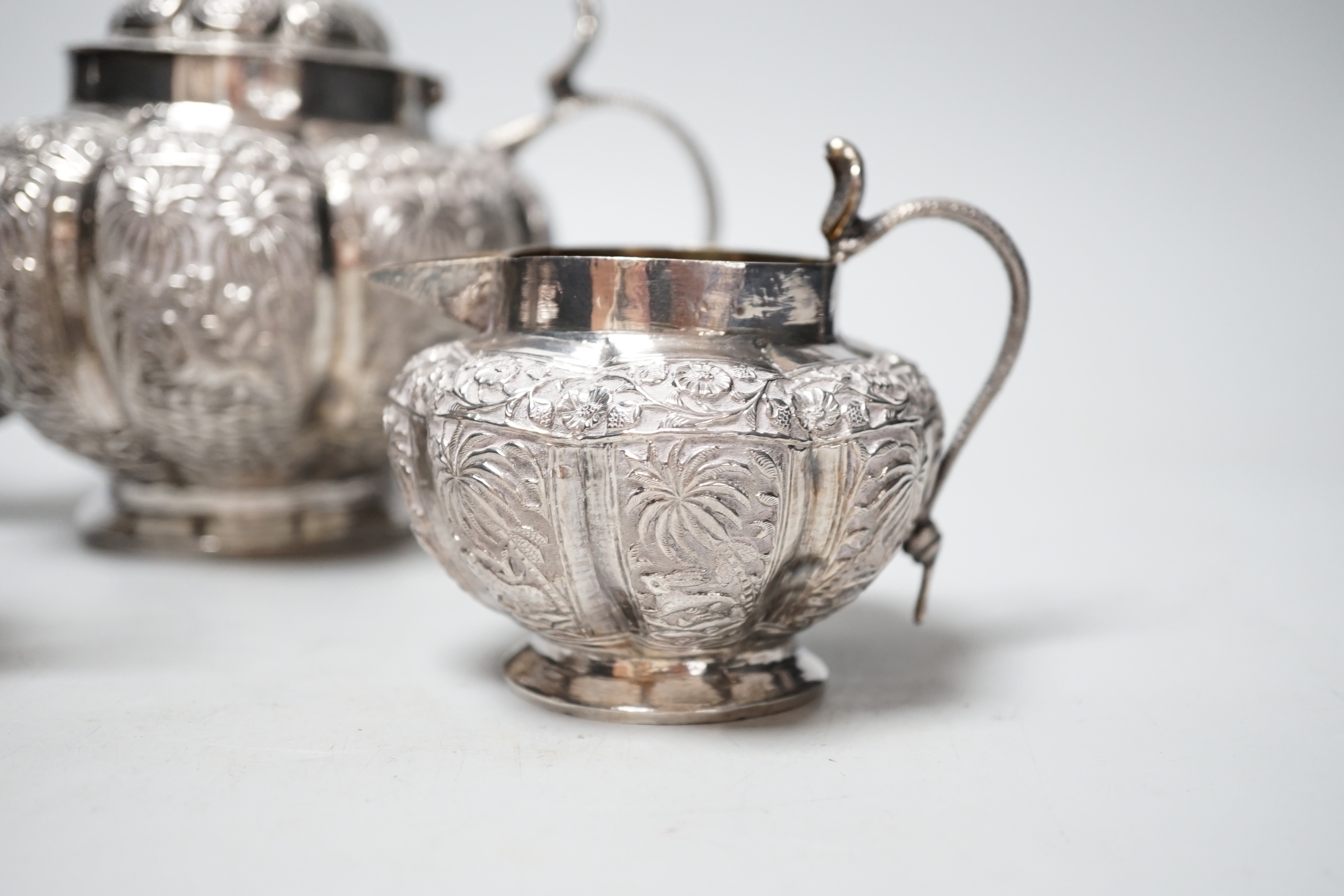 An Indian embossed white metal three piece tea set, with cobra handles and elephant finial, 25.7oz.